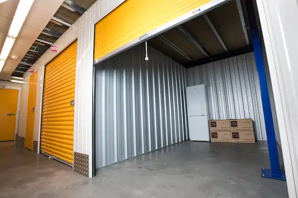 Box de stockage avec rideau jaune ouvert, contenant un frigo et des cartons Atout-Box soigneusement rangés.