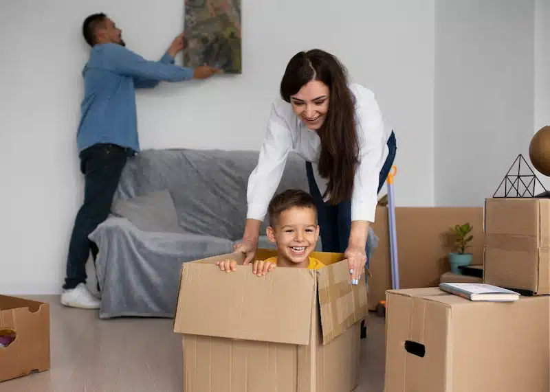 Parents qui déménagent avec leur enfant, qui s'amuse dans les cartons. 