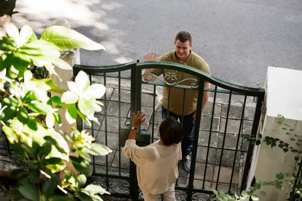 Deux voisins se saluant à travers un portail. 