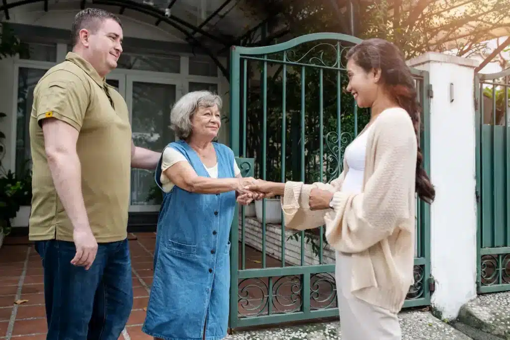 Rencontre en des voisins en face d'un portail. Un homme et deux dames se serrant la main.