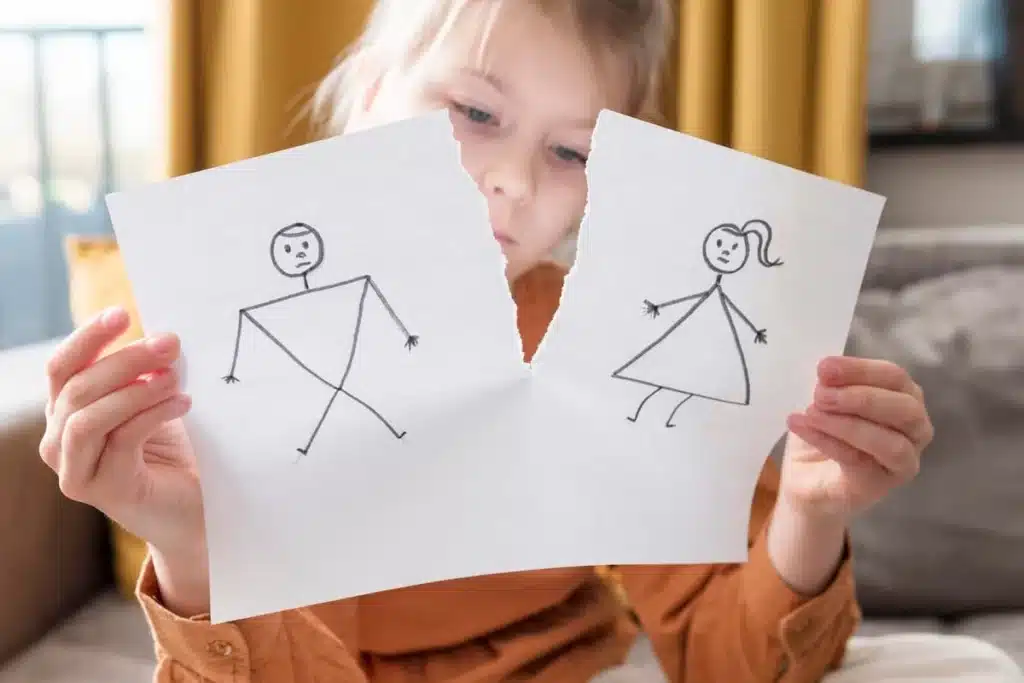 Enfant tenant dans ses mains une feuille déchirée en deux, sur laquelle d'un côté est dessiné un homme de l'autre une femme, pour représenter la séparation. 