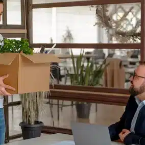 Un homme debout tient un carton rempli, son collègue le regarde.