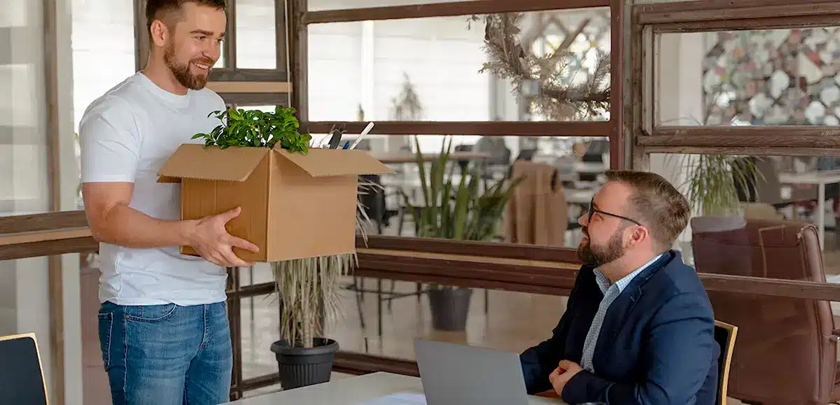 Un homme debout tient un carton rempli, son collègue le regarde.