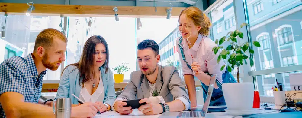 4 professionnels sont en réunions, ils regardent un téléphone.