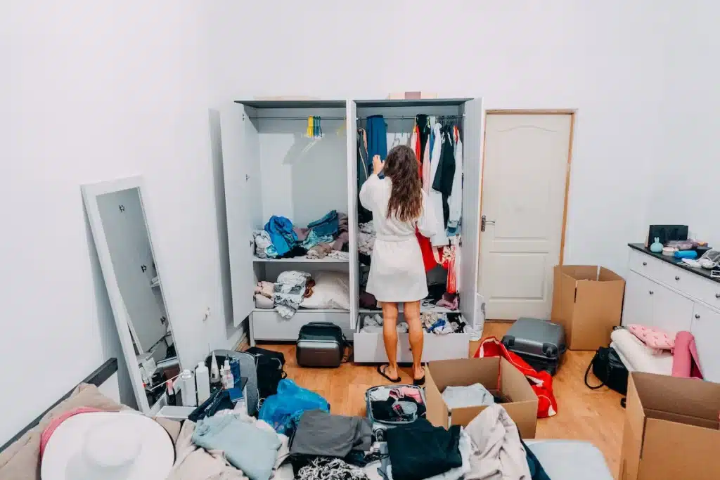 Chambre d'une femme qui semble trier les vêtements de sa penderie. 