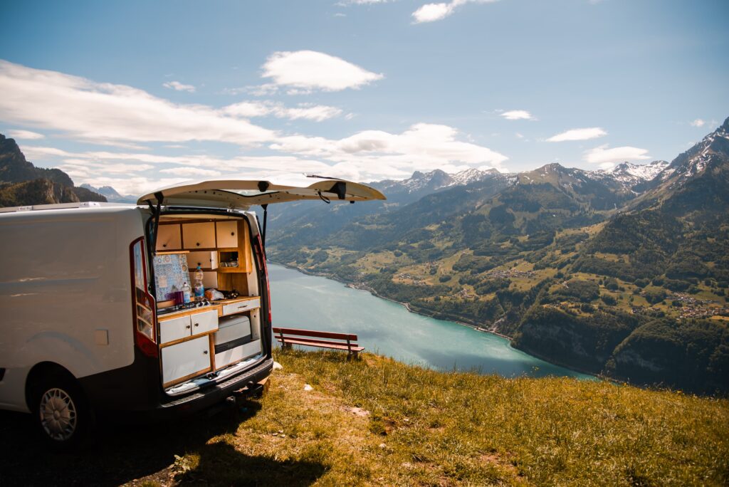 Fourgon aménagé ouvert à l’arrière, offrant une vue panoramique sur un lac et des montagnes majestueuses.