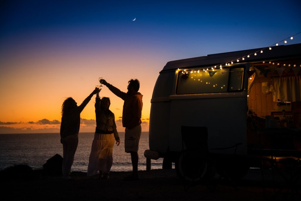 Amis réunis autour d’un feu de camp près de leur van, au coucher du soleil. Une scène qui donne envie de tout plaquer pour vivre dans un van.