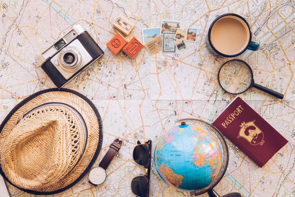 carte du monde avec différents objets dessus tels que : un appareil photo, une loupe, un passeport, des lunettes de soleil, une montre, un chapeau, des timbres, une tasse et un globe terrestre