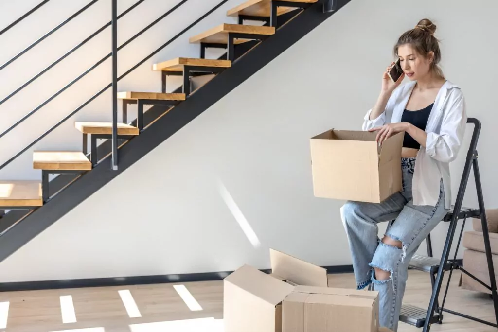photo d'une femme au téléphone entrain de trier ses cartons à côté d'un escalier 